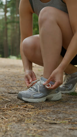 Vídeo-Vertical-De-Cerca-De-Una-Mujer-Atándose-Los-Cordones-De-Una-Zapatilla-Deportiva-Antes-De-Hacer-Ejercicio-Corriendo-Por-Una-Pista-A-Través-De-Un-Bosque,-Filmado-En-Tiempo-Real-1